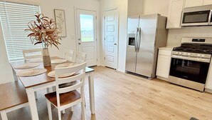 Una cocina moderna con armarios blancos, electrodomésticos de acero inoxidable y un comedor con mesa de madera y sillas blancas.
