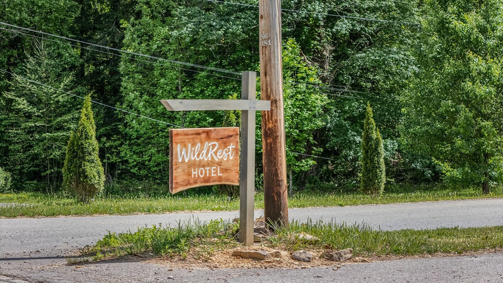Un letrero de madera del Hotel WildRest, con un diseño rústico, situado al lado de una carretera con un fondo de vegetación densa.