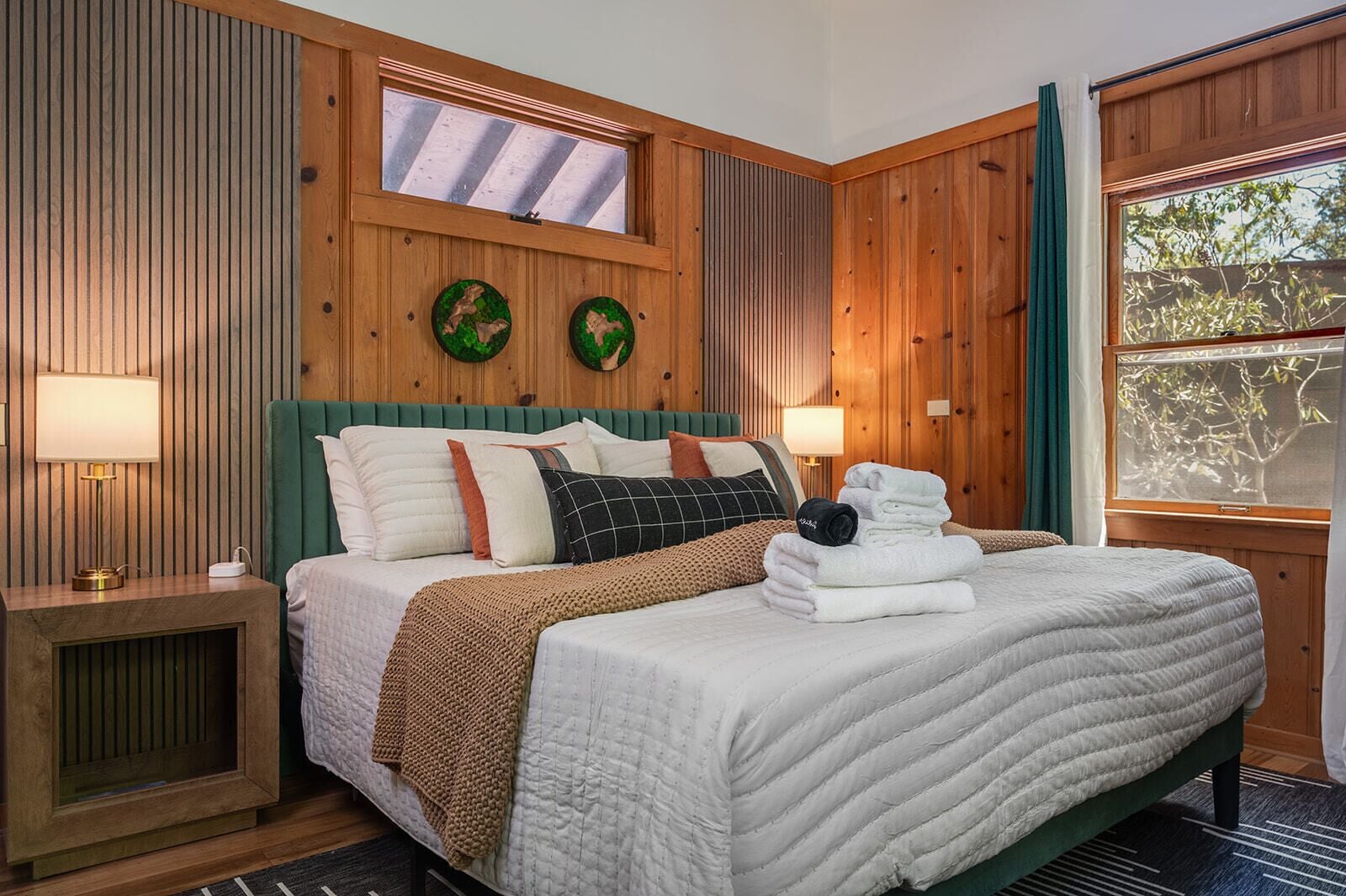 Quarto com cama, duas relógios fixados na parede, janela com cortinas e um painel de parede de madeira.
