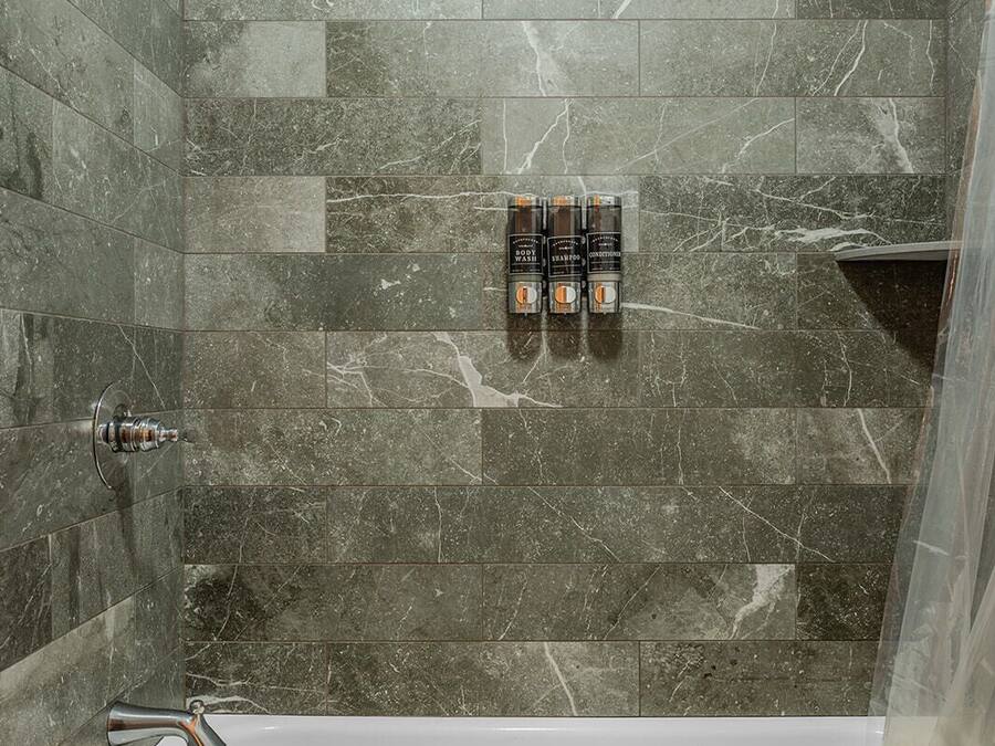 A bathroom with a white bathtub, a showerhead, and three body wash bottles on the wall.