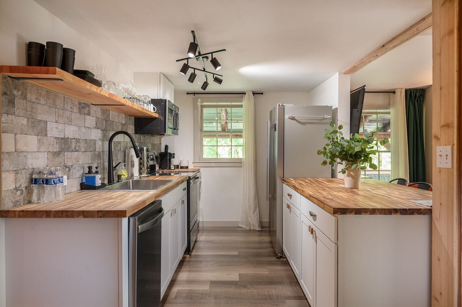 A narrow kitchen with a wooden countertop, a built-in oven, a refrigerator, and a potted plant.