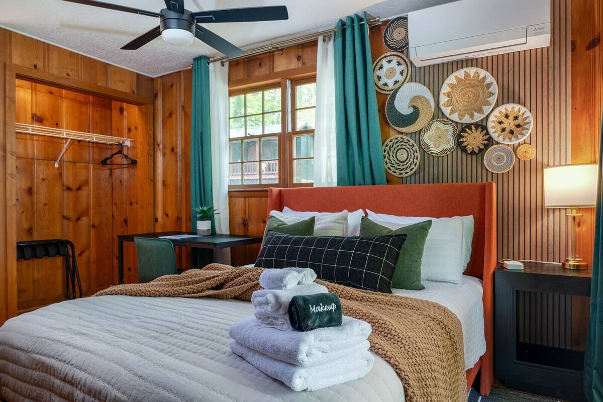 A cozy room with a bed, a table, a chair, a ceiling fan, and a window with curtains.
