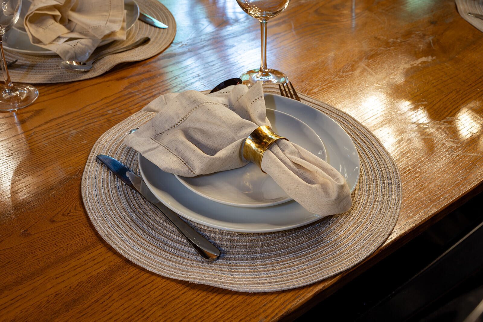A dining table with a plate, napkin, fork, and knife set on a woven placemat.