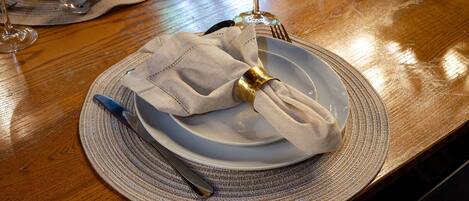 A dining table with a plate, napkin, fork, and knife set on a woven placemat.