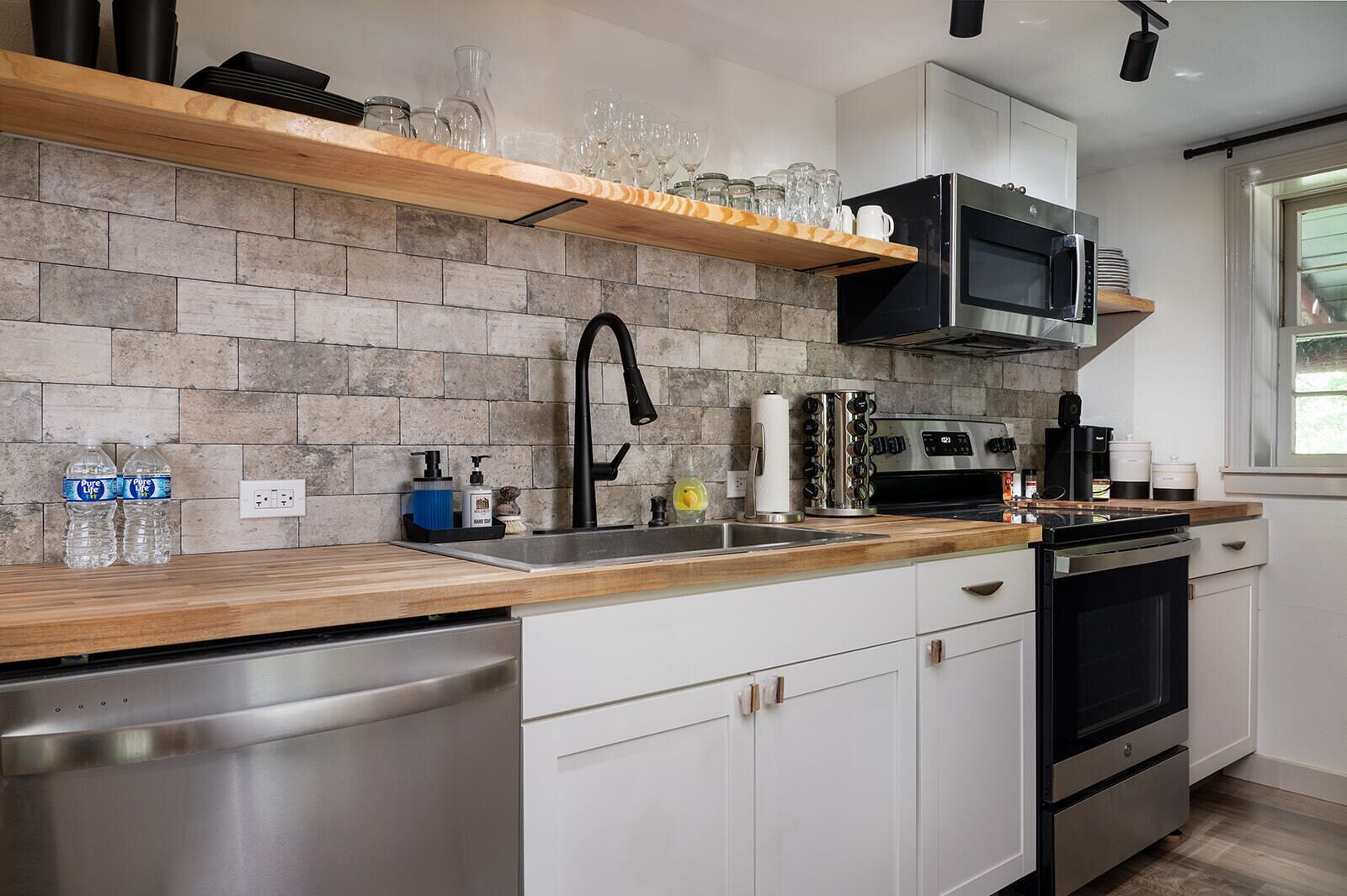 A modern kitchen with a stone backsplash, stainless steel appliances, and a wooden countertop.