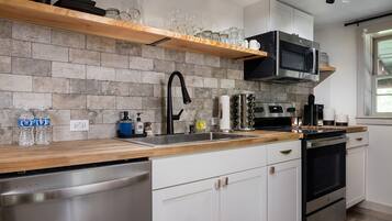 A modern kitchen with a stone backsplash, stainless steel appliances, and a wooden countertop.