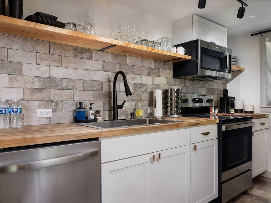 A modern kitchen with a stone backsplash, stainless steel appliances, and a wooden countertop.