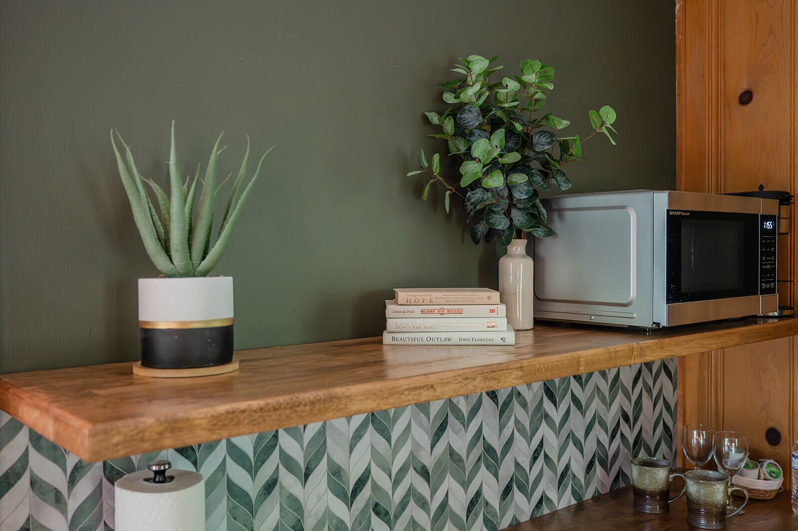 A kitchen counter with a microwave, a potted plant, a stack of books, and a patterned backsplash.