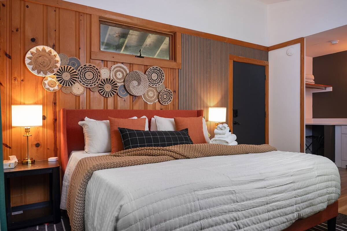 A hotel room with a large bed, wooden panel walls, a television, and a window with blinds.