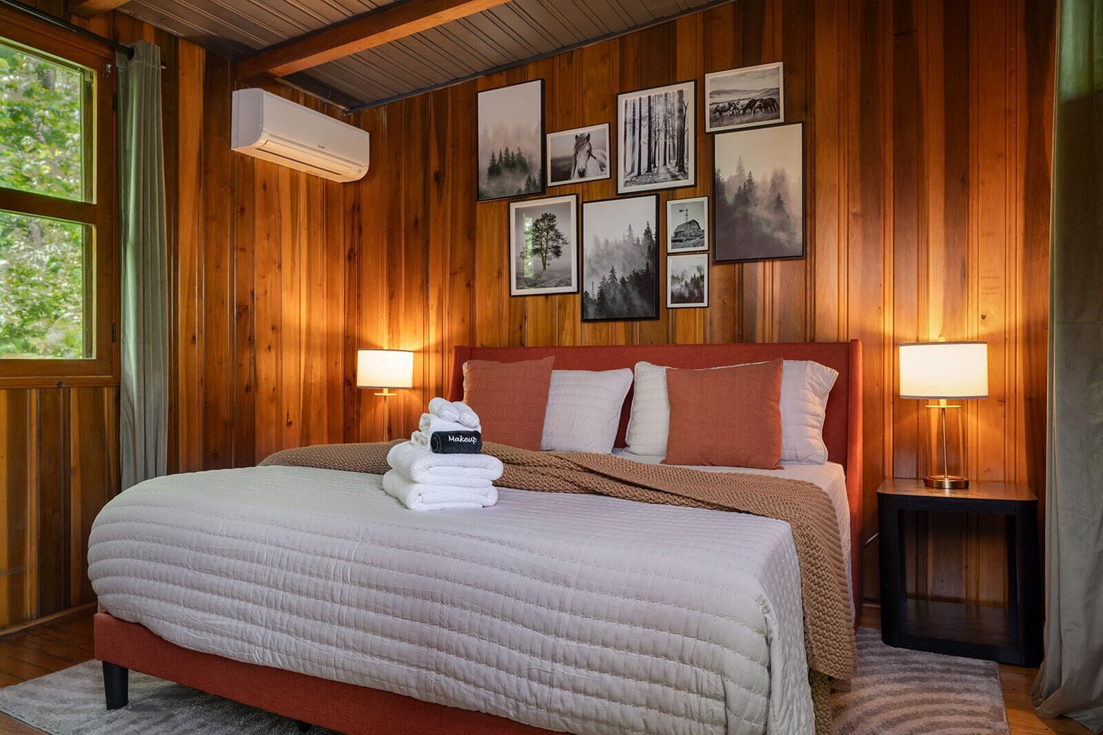 Een kamer met houten lambrisering, een bed, twee bedlampen en een muur met ingekaderde foto's.