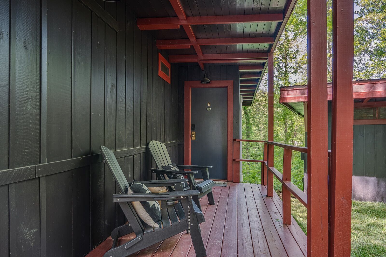A covered porch with wooden railings, a door, and two Adirondack chairs.
