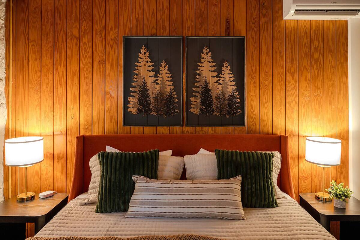 A bed with a headboard, two wall-mounted lamps, and two framed pictures of trees.
