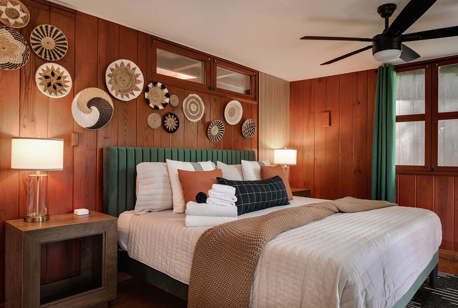 A wooden-paneled room with a bed, two bedside tables, a ceiling fan, and wall-mounted decor.