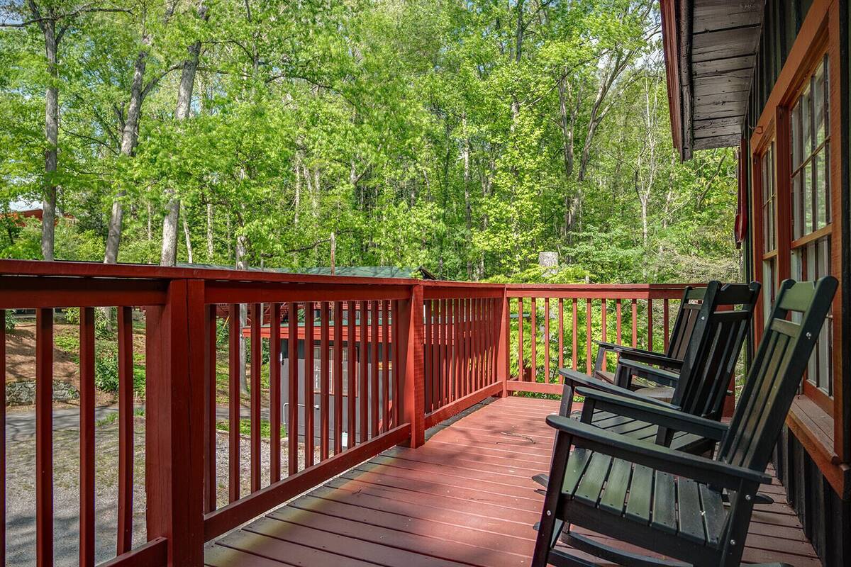 A wooden deck with red railings, surrounded by trees.