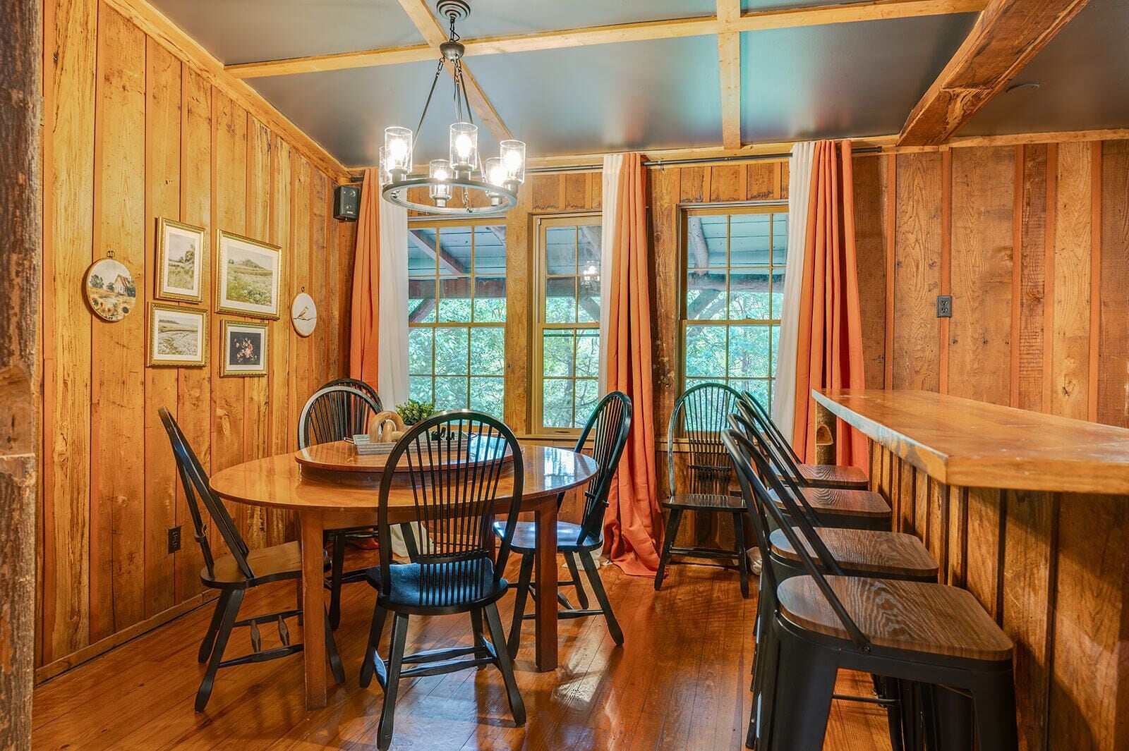 A wooden-paneled room with a round table, chairs, a bar, and framed pictures on the walls.