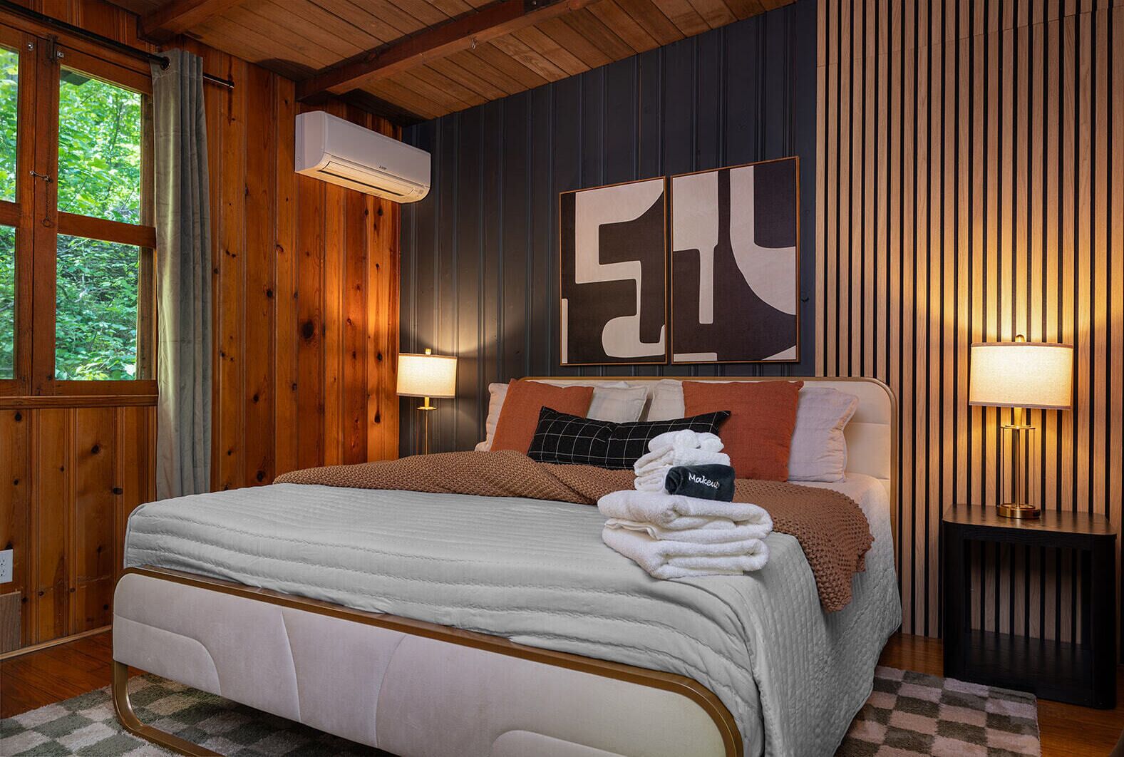 Una camera da letto con un letto, un condizionatore d'aria a parete, un grande quadro astratto e una lampada da comodino.