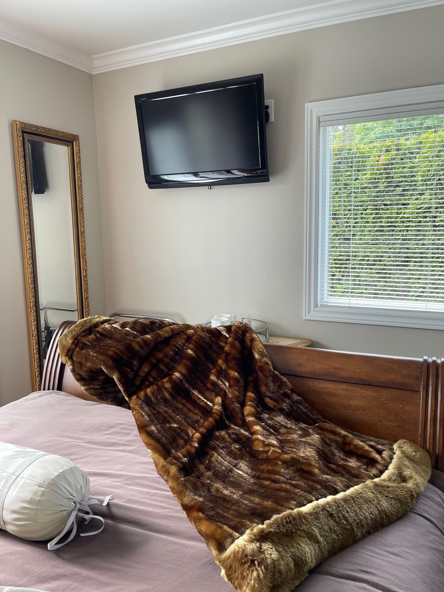 Een slaapkamer met een bed, een aan de muur bevestigde televisie, een raam met zonwering en een spiegel.