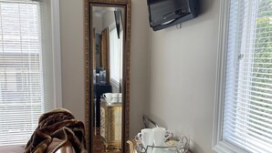 A room with a wooden floor, a sofa, a small cabinet with decorative patterns, a television mounted on the wall, and a large mirror. - Snowbird Delight (Victoria)