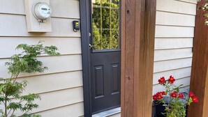 A house entrance with a black door, a utility meter, a potted plant, and a flower pot. - Snowbird Delight (Victoria)