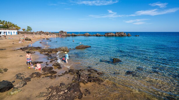 A beach with clear water, rocks, and a few people. - Casa Apolo (Puerto del Carmen)