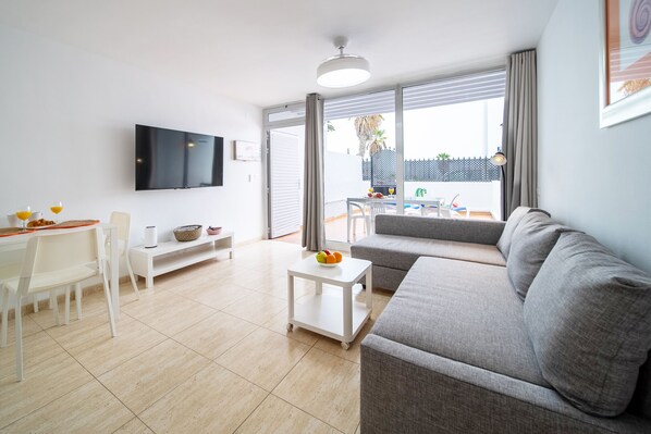A modern living room with a grey sofa, a white coffee table, and a TV mounted on the wall.