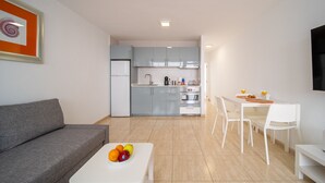 A modern living room with a grey sofa, a white coffee table with fruit, and a dining area with white chairs and a table. - Casa Apolo (Puerto del Carmen)
