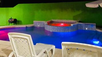 Una piscina con hidromasaje, rodeada por un muro verde y una terraza con baldosas.
