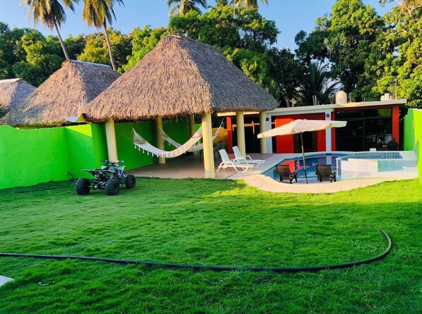 Un complexe hôtelier doté de bâtiments à toits de chaume, d’une piscine et d’une pelouse verdoyante.
