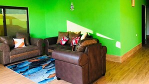 Un salon avec un mur vert, deux canapés marron, une table basse et un tapis.