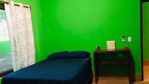 Une chambre avec deux lits, une table de chevet en bois, un mur vert et une fenêtre avec des rideaux.