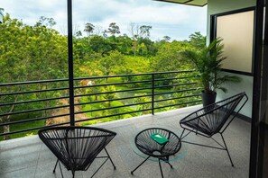 A balcony with a view of a lush green landscape, two black wireframe chairs, and a small table with a green book.