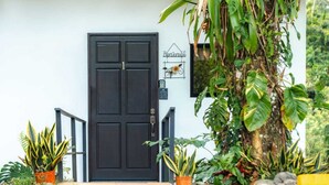 Una puerta negra con buzón y cartel de bienvenida, rodeada de macetas con plantas.