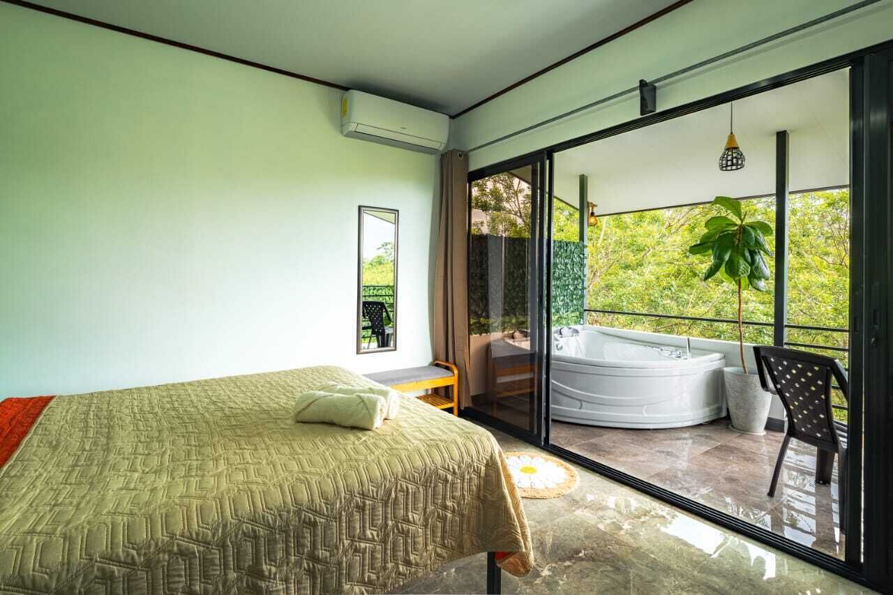 A bedroom with a bed, a window, and a balcony with a hot tub.