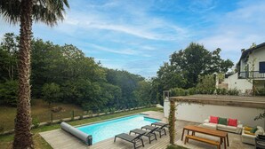 Un patio trasero con piscina, terraza de madera y mobiliario exterior.