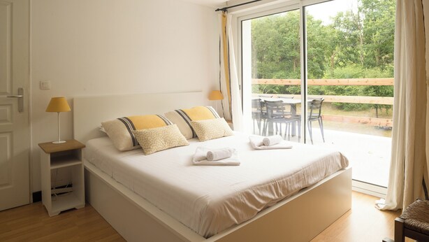 Un dormitorio con una cama grande, una mesita de noche, una lámpara y vistas a un patio exterior con sillas y una mesa.