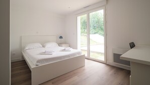 Un dormitorio moderno con una cama grande, un escritorio y un ventanal corredera que da a un balcón.