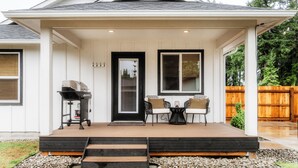 A covered porch with a grill, two chairs, and a table.