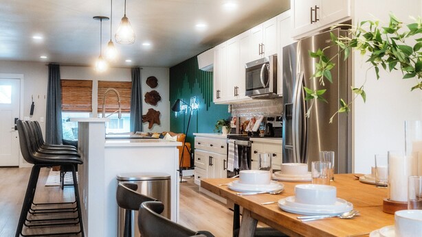 A modern kitchen with white cabinets, a stainless steel refrigerator, and a wooden dining table set for four.