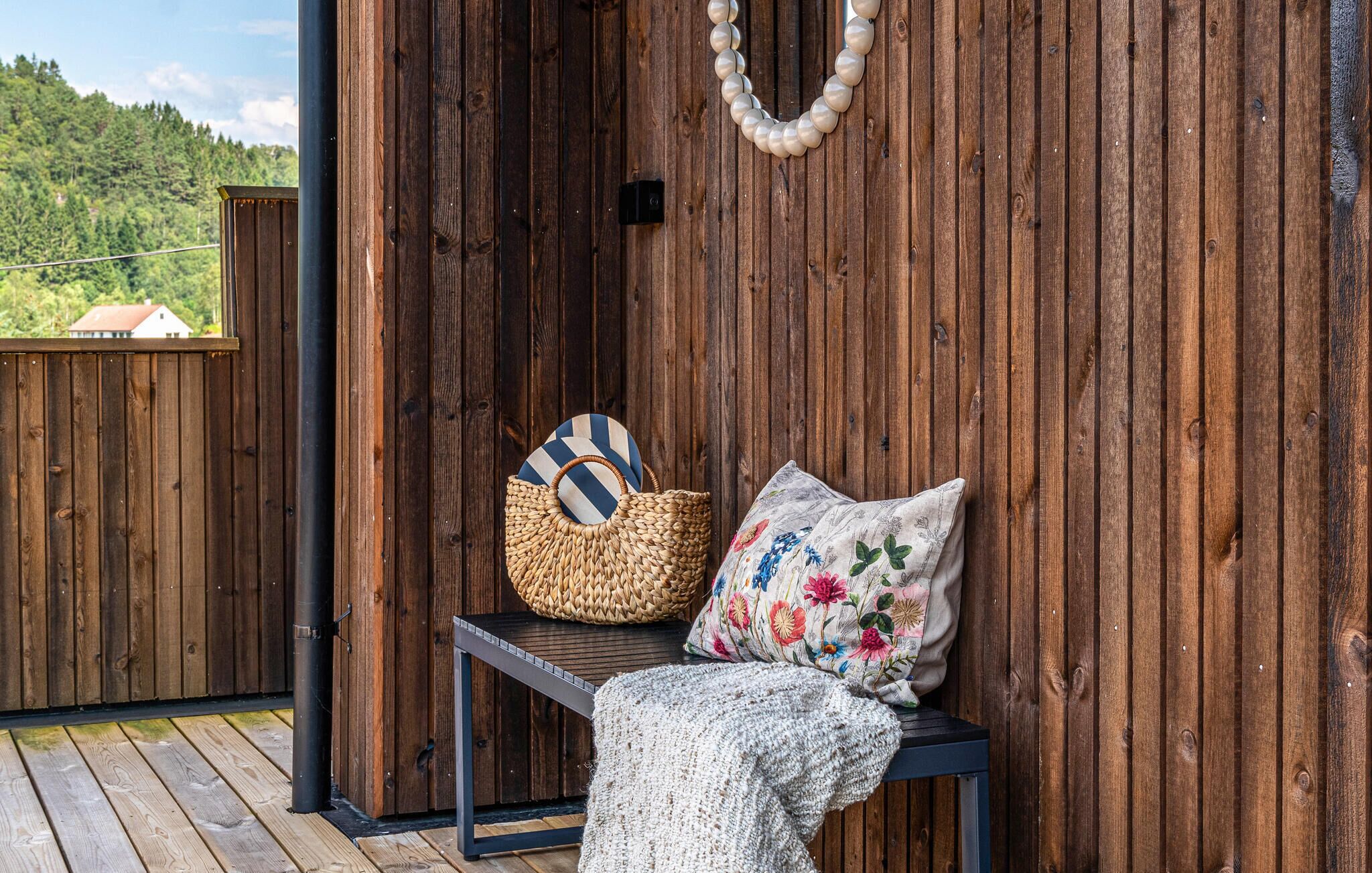 Un banc en bois, avec un panier tressé et un coussin à motifs floraux, adossé à un mur en bois.