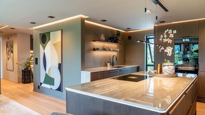 A modern kitchen with a central island, built-in shelves, and a large abstract painting on the wall.