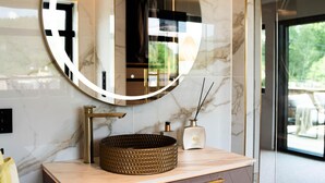 A bathroom with a round mirror, a gold-colored sink, and a marble wall.