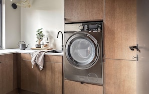 A compact, modern laundry room with a built-in washer and dryer, wooden cabinets, a small sink, and a window with natural light. - Luxurious home in Ytre Arna with WiFi (Ytre Arna)