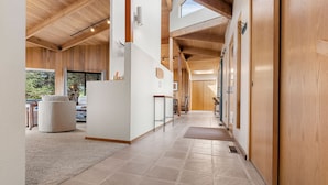 Un hall spacieux avec des poutres en bois, un plafond haut et une lucarne. On y trouve un coin salon avec un fauteuil confortable et une table.