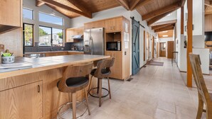Une cuisine moderne avec des meubles en bois, un îlot central doté de tabourets de bar et une grande fenêtre qui laisse entrer la lumière naturelle.