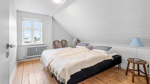 Ein Schlafzimmer mit schrägen Wänden, einem Bett mit schwarzem Gestell, Holzboden, einem Fenster mit Jalousien und einer Nachttischlampe.