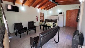 Ein großzügiger Wohnbereich mit hoher Decke, Holzbalken, einem Esstisch mit Stühlen, einer Couch und einem an der Wand befestigten Fernseher.