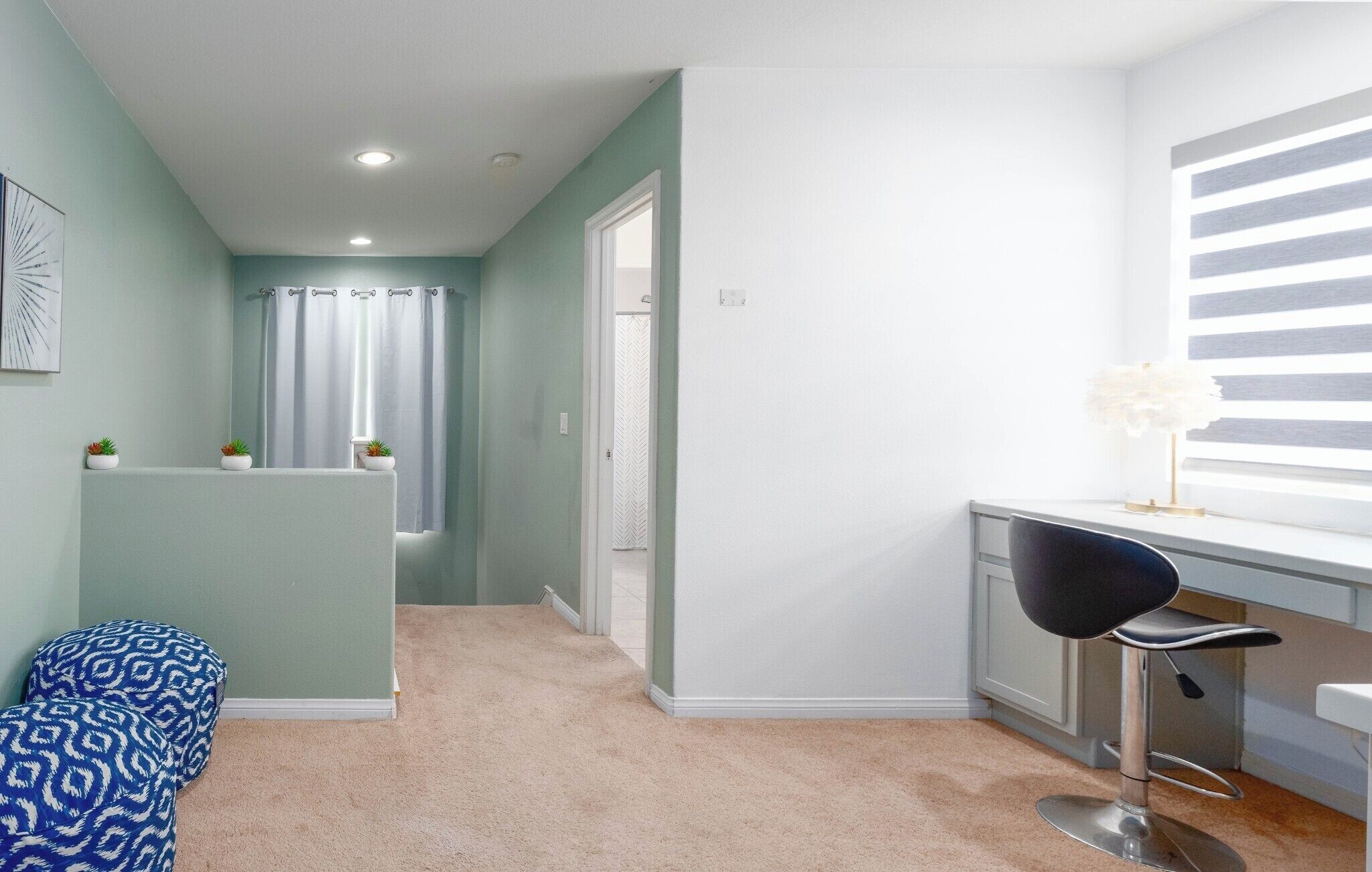 A narrow hallway with a light green wall, a white door, and a small seating area with a patterned ottoman.