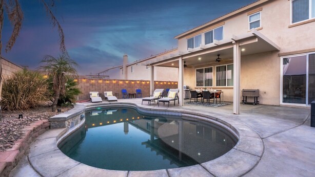 Un jardin avec une piscine, des chaises longues, un espace barbecue et une terrasse couverte.