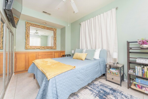 A bedroom with a bed, a nightstand, a bookshelf, a mirror, and a window with curtains.