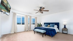 Une chambre à coucher comprenant un lit, un ventilateur de plafond, une table de chevet, un banc et une fenêtre avec des rideaux.